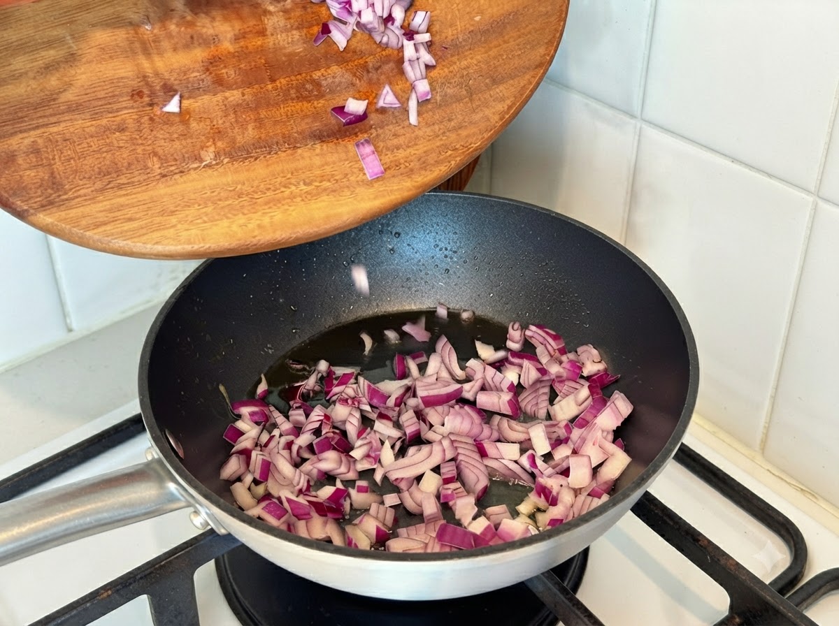 Gehackte rote Zwiebeln werden von einem Holzbrett in eine heiße Bratpfanne mit Öl gegeben.