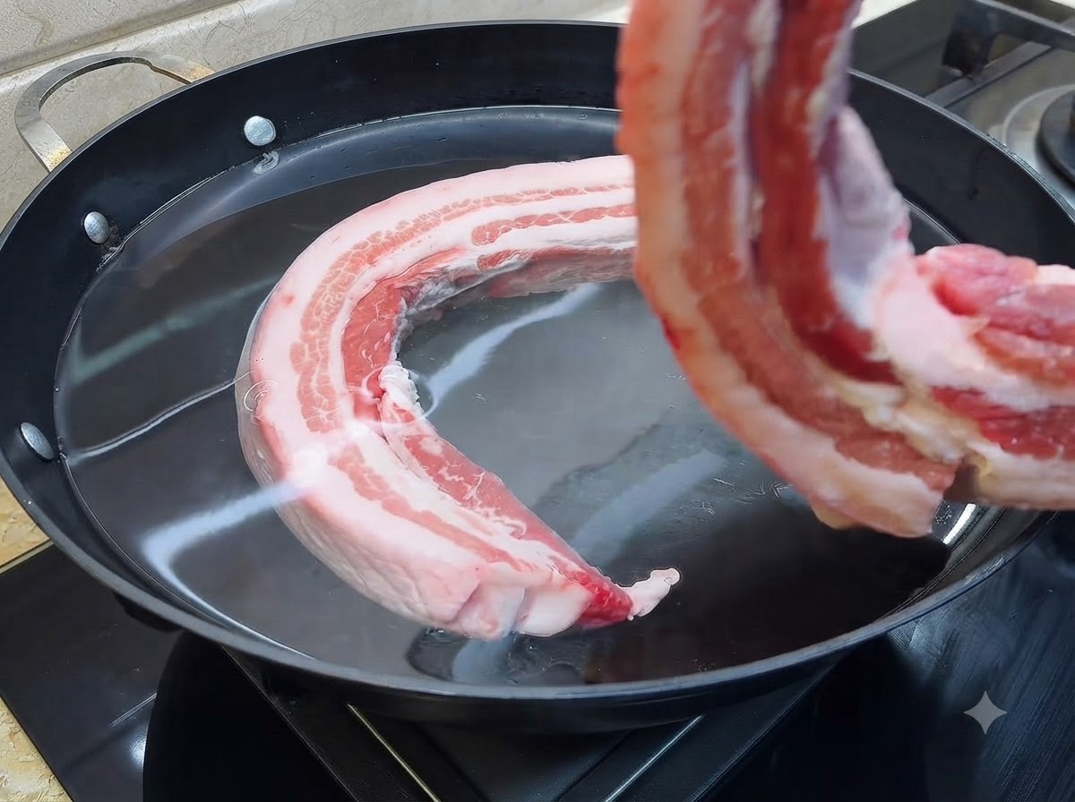 Ein Stück roher Schweinebauch wird in einen großen Topf mit kaltem Wasser gegeben.