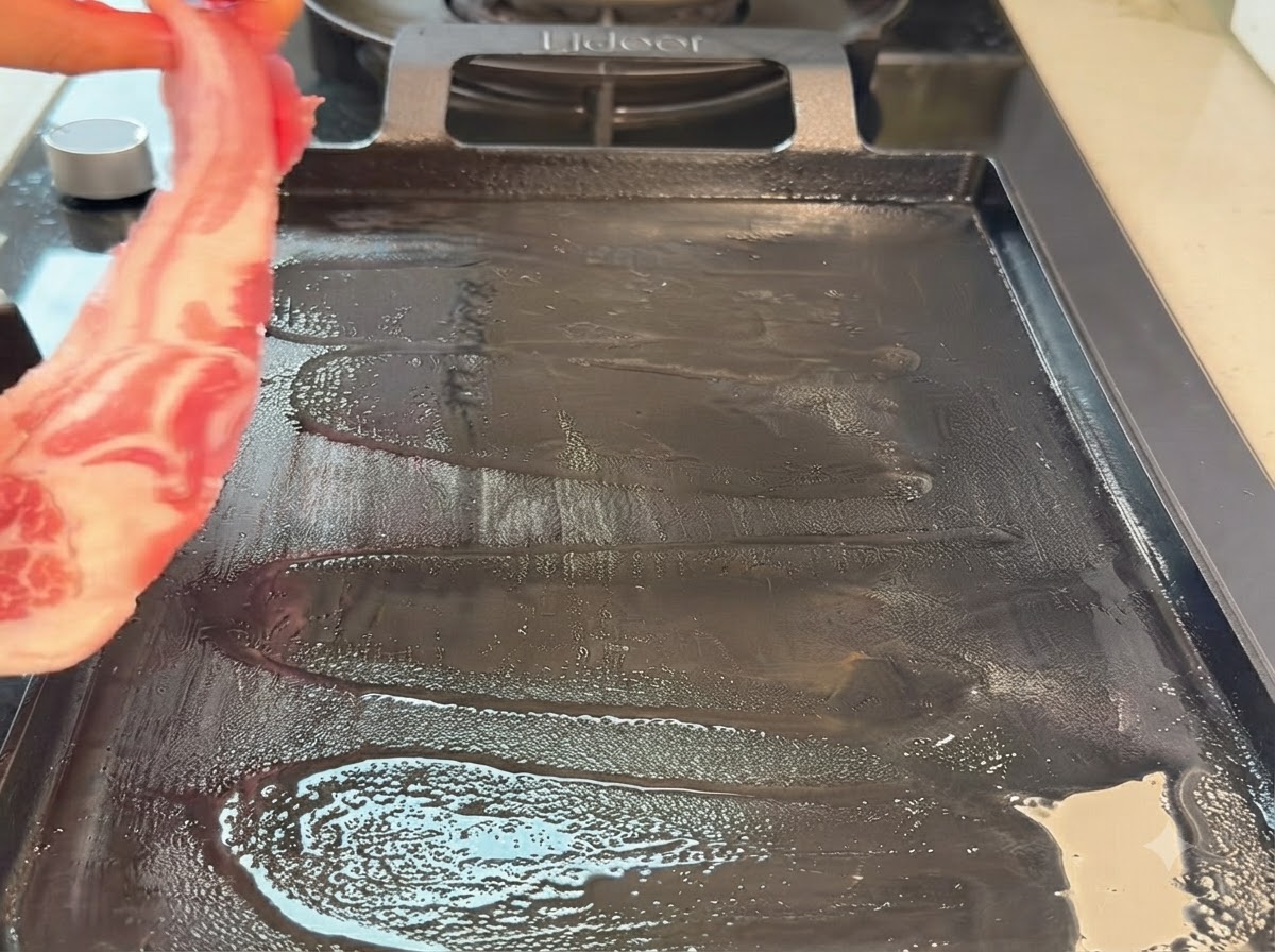 Ein roher Schweinebauchstreifen wird auf eine heiße Teppanyaki-Grillpfanne gelegt.