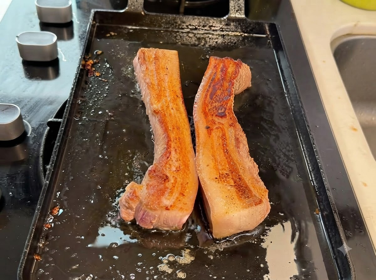 Dicke Schweinebauchstreifen werden mit einer Küchenschere auf der Grillpfanne in kleinere Stücke geschnitten.