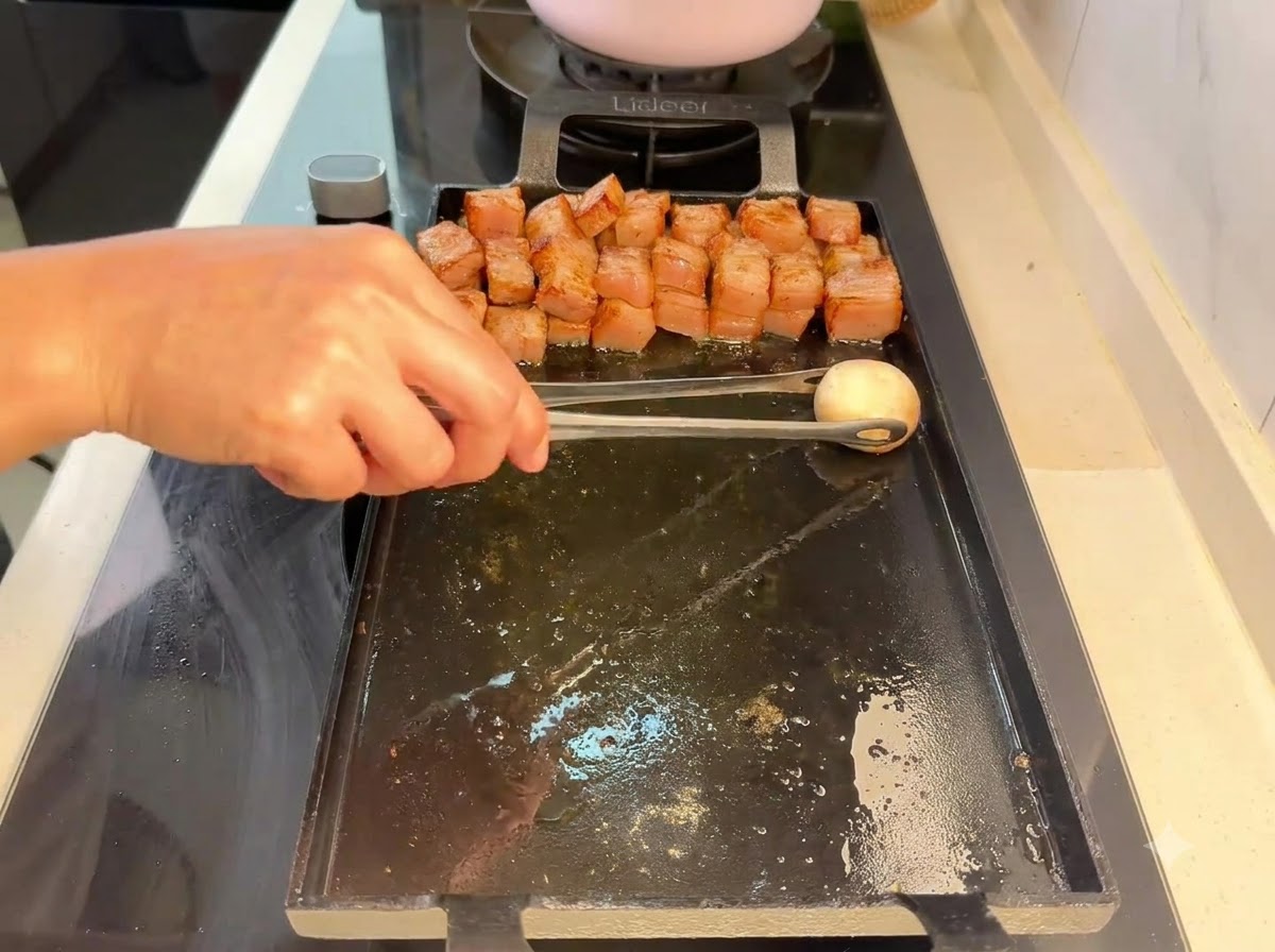 Ein Champignon wird mit einer Zange neben gegrillten Fleischstücken auf den Grill gelegt.