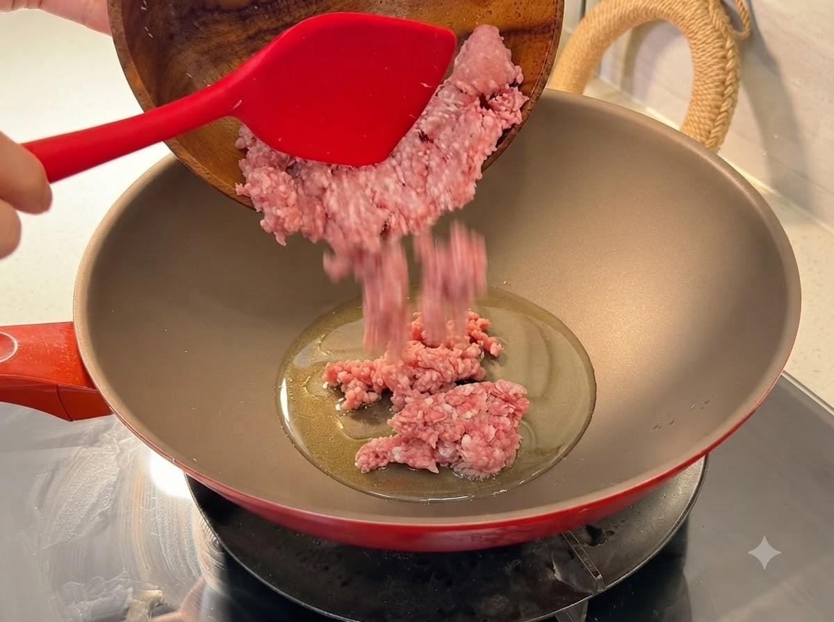 Frisches Hackfleisch wird aus einer Holzschüssel in einen beheizten roten Wok mit Öl gegeben.