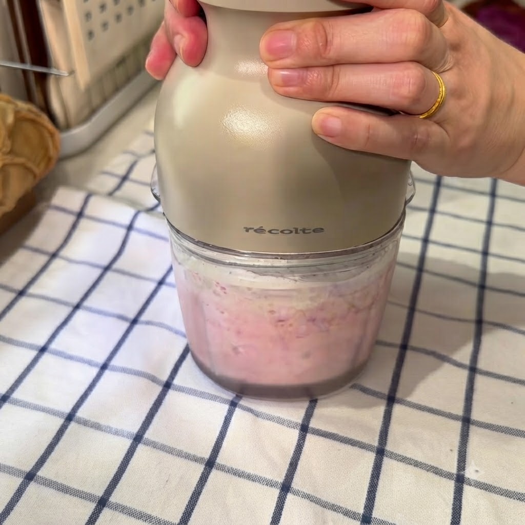 Eine Küchenmaschine mixt eine rosa Mischung aus gefrorener Wassermelone, Eiswasser und Kondensmilch.