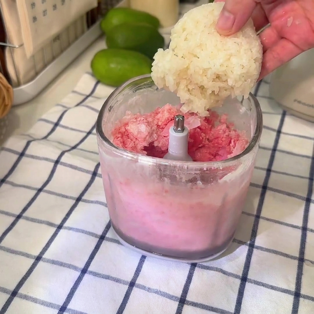 Eine Kugel Klebreis wird in einen klaren Mixerbecher mit rosa Wassermelonen-Slushie-Mischung gegeben.