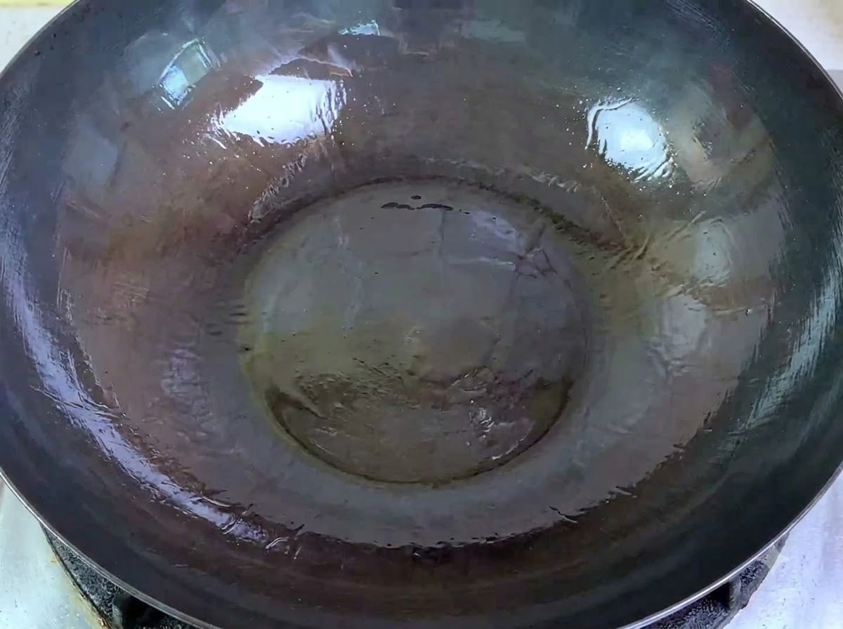 Rohes Schweinehackfleisch wird aus einer Schüssel in einen großen Wok mit heißem Öl gegeben.