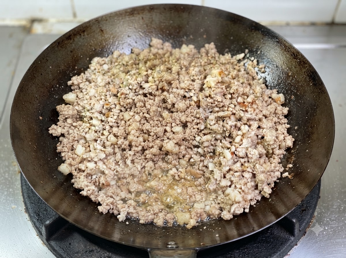 Schweinehackfleisch bräunt in einem Wok mit sichtbarem, sprudelndem Fett am Boden.