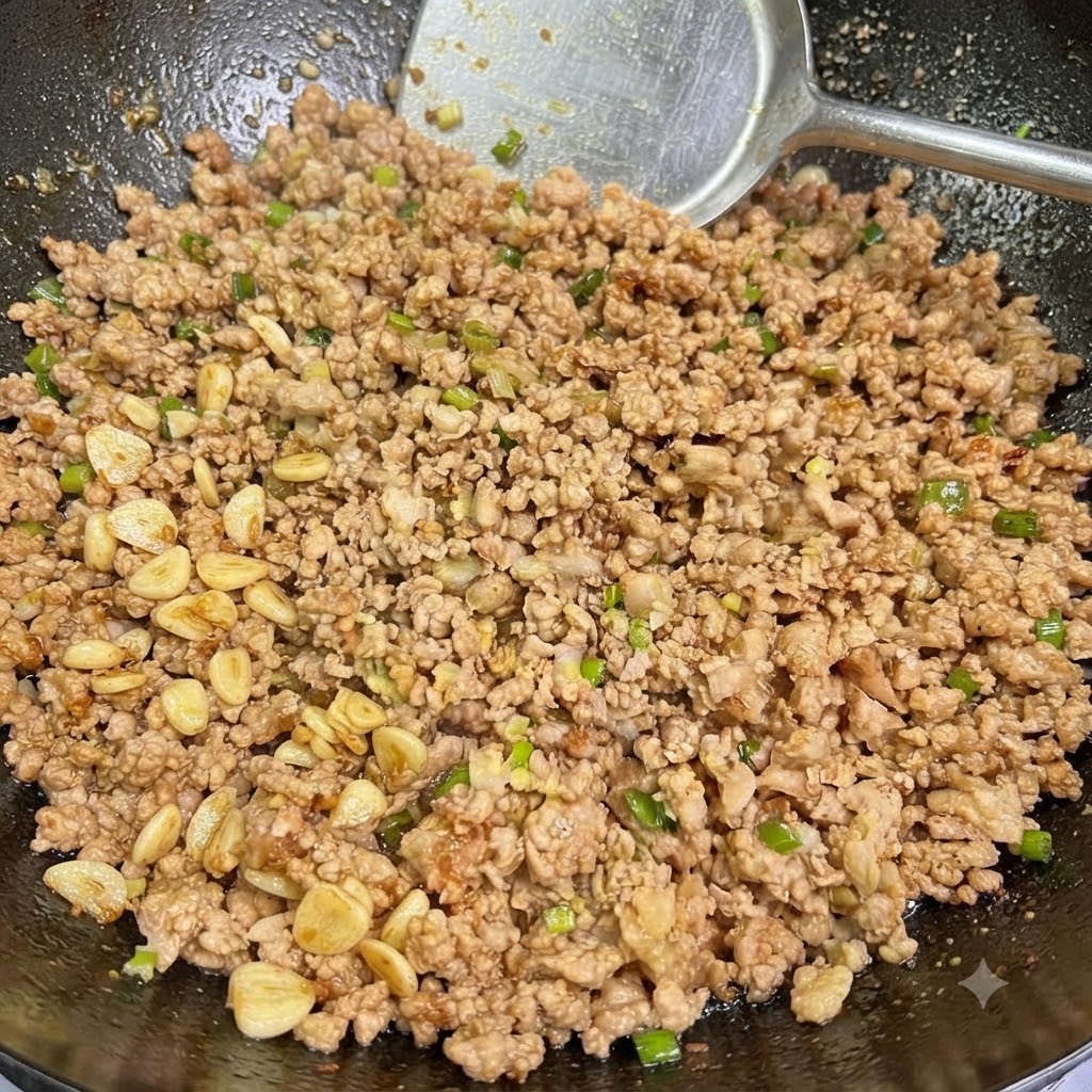 Gegartes Schweinehackfleisch vermischt mit Frühlingszwiebeln und Knoblauch wird in einem Wok mit einem Pfannenwender umgerührt.