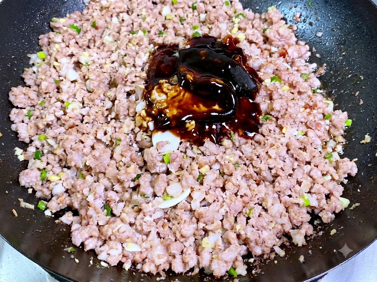 Ein Haufen dunkler Sojabohnenpasten und Saucen liegt direkt auf dem gegarten Schweinehackfleisch in einem Wok.
