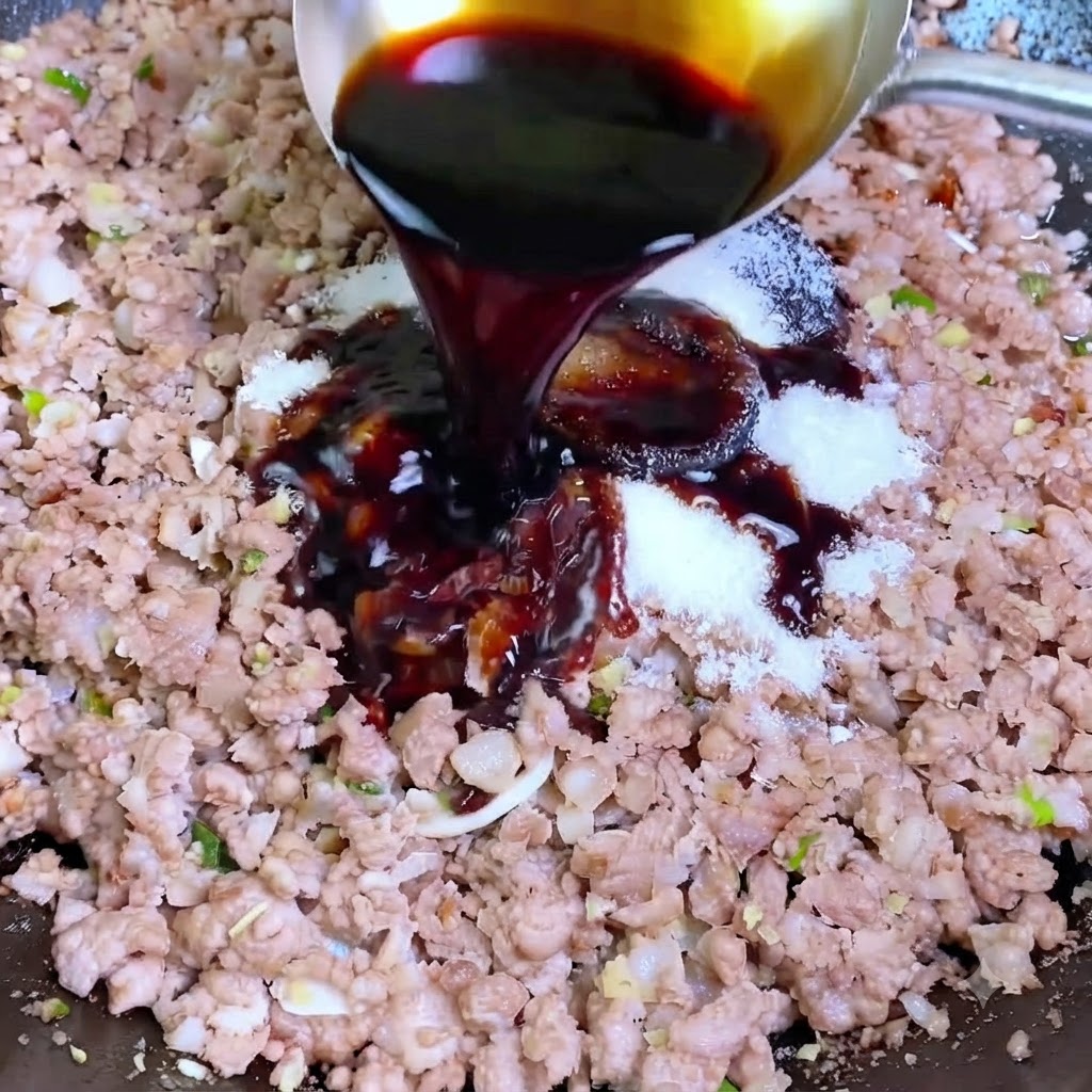 Dunke Sojasauce wird aus einer silbernen Kelle in einen Wok mit Schweinehackfleisch und weißen Gewürzen gegossen.