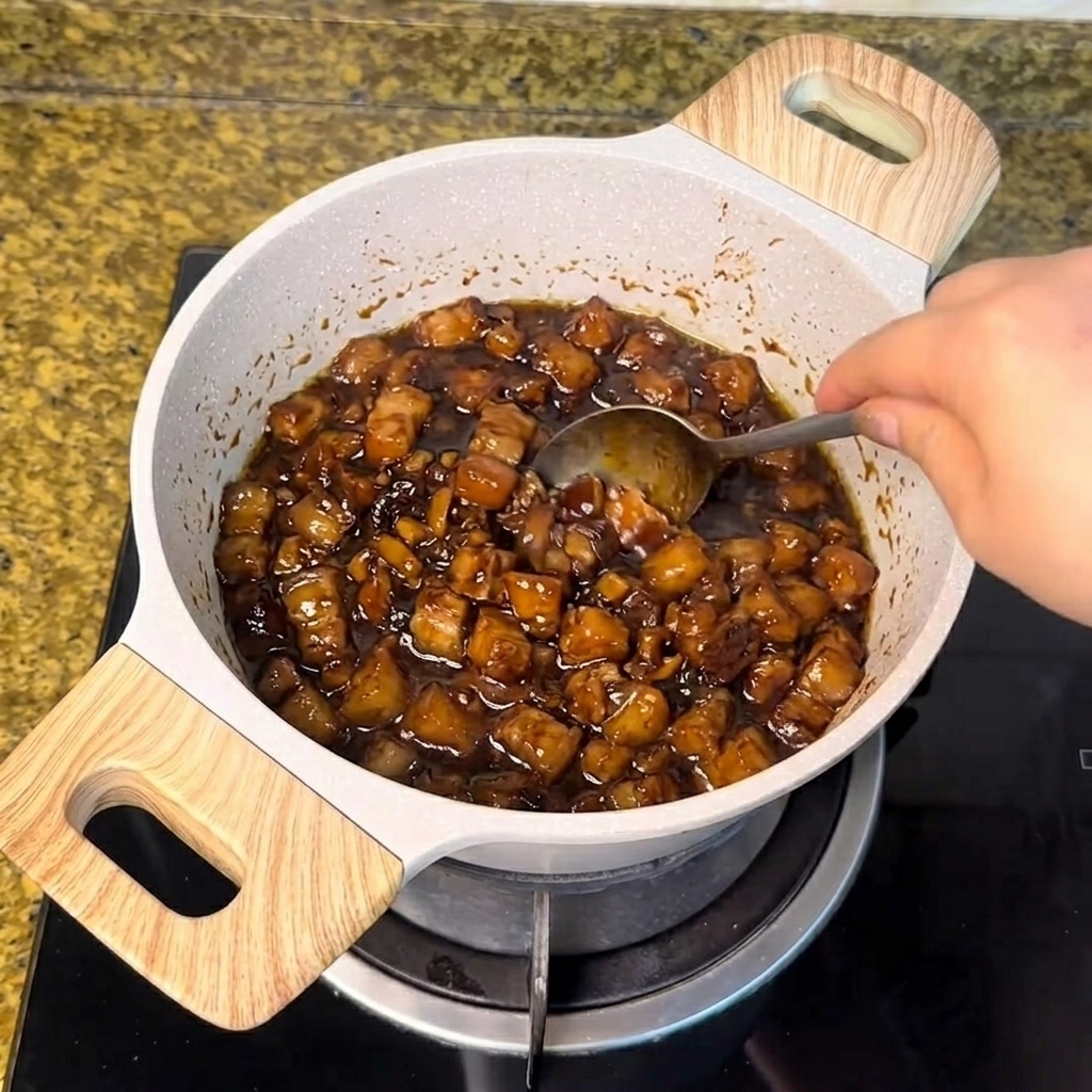Weißer Zucker wird mit einem Löffel in die köchelnde dunkle Fleischsauce gerührt.