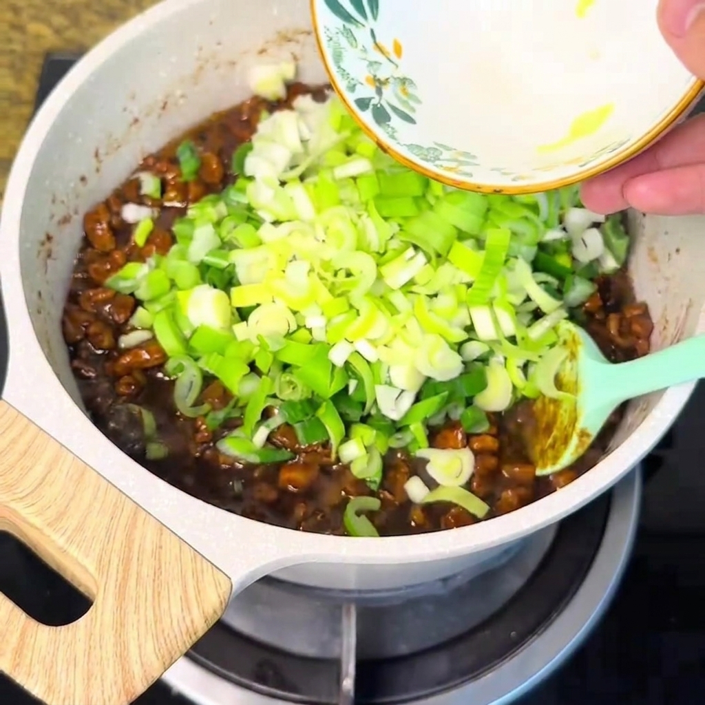 Gehackte Frühlingszwiebeln werden aus einer Schüssel in die blubbernde Fleischsauce geschüttet.