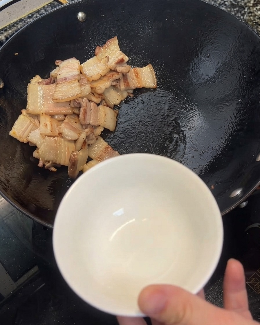 Überschüssiges Öl wird mit einem Pfannenwender aus dem Wok in eine weiße Schüssel geschöpft.