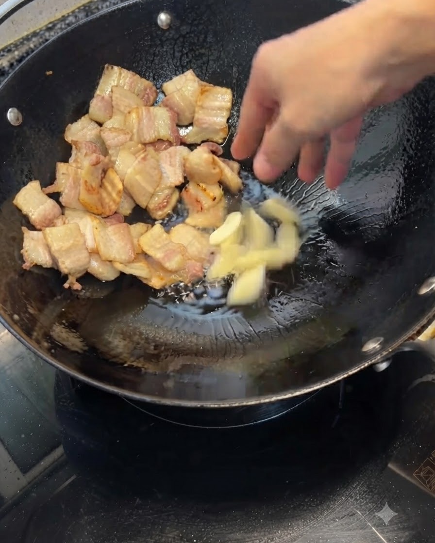 Zerkleinerte Knoblauchzehen werden in einen Wok mit gebratenen Schweinebauchstückchen gegeben.
