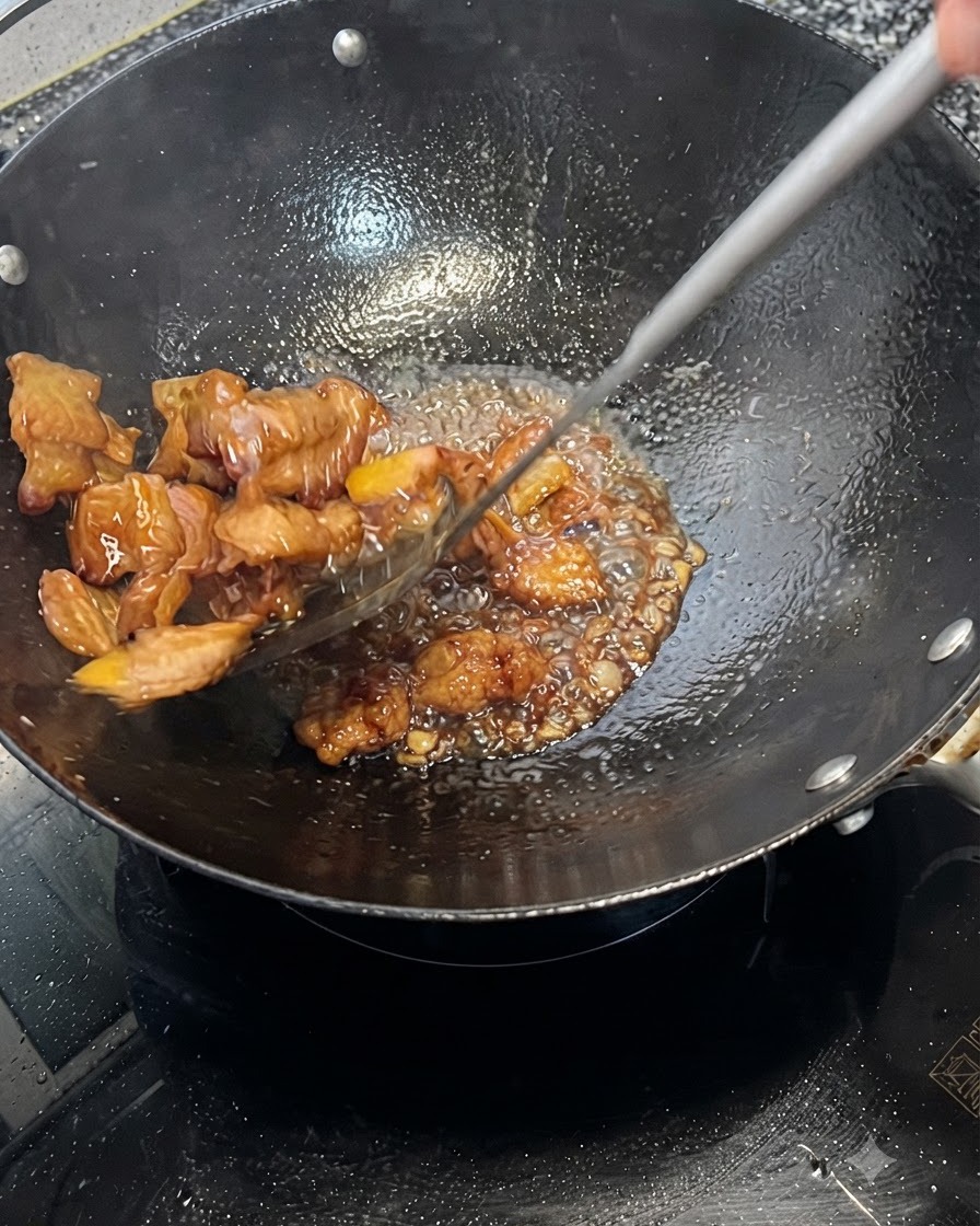 Schweinebauch wird in einem Wok schnell in einer blubbernden dunklen Sauce gewendet und überzogen.