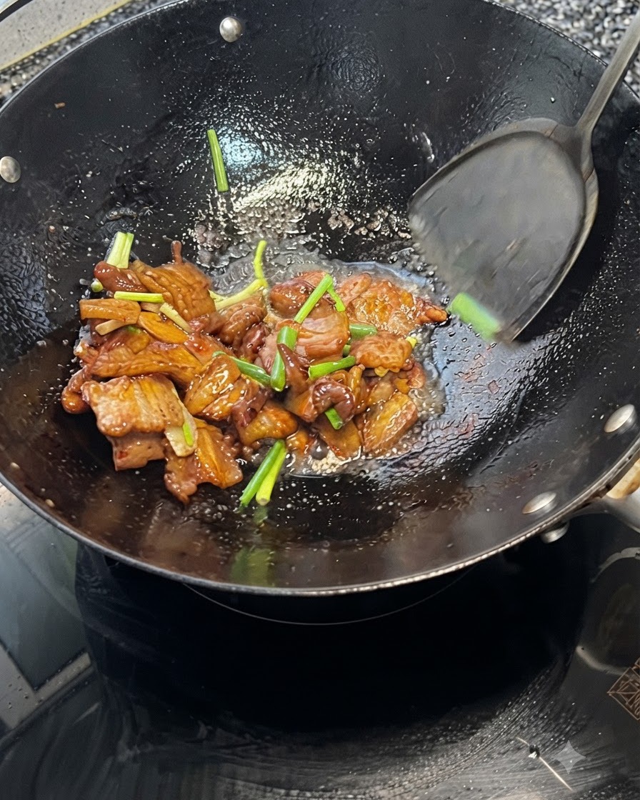 Ein Pfannenwender schwenkt Schweinebauch und Frühlingszwiebeln zusammen in einem heißen Wok.