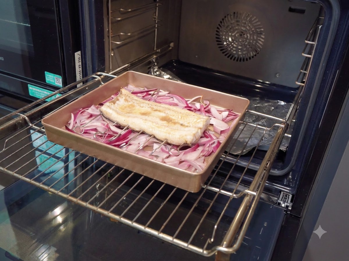 Ein Pinsel trägt eine dicke, dunkelbraune Sauce auf ein vorgebackenes Aalfilet in einer Backform auf.