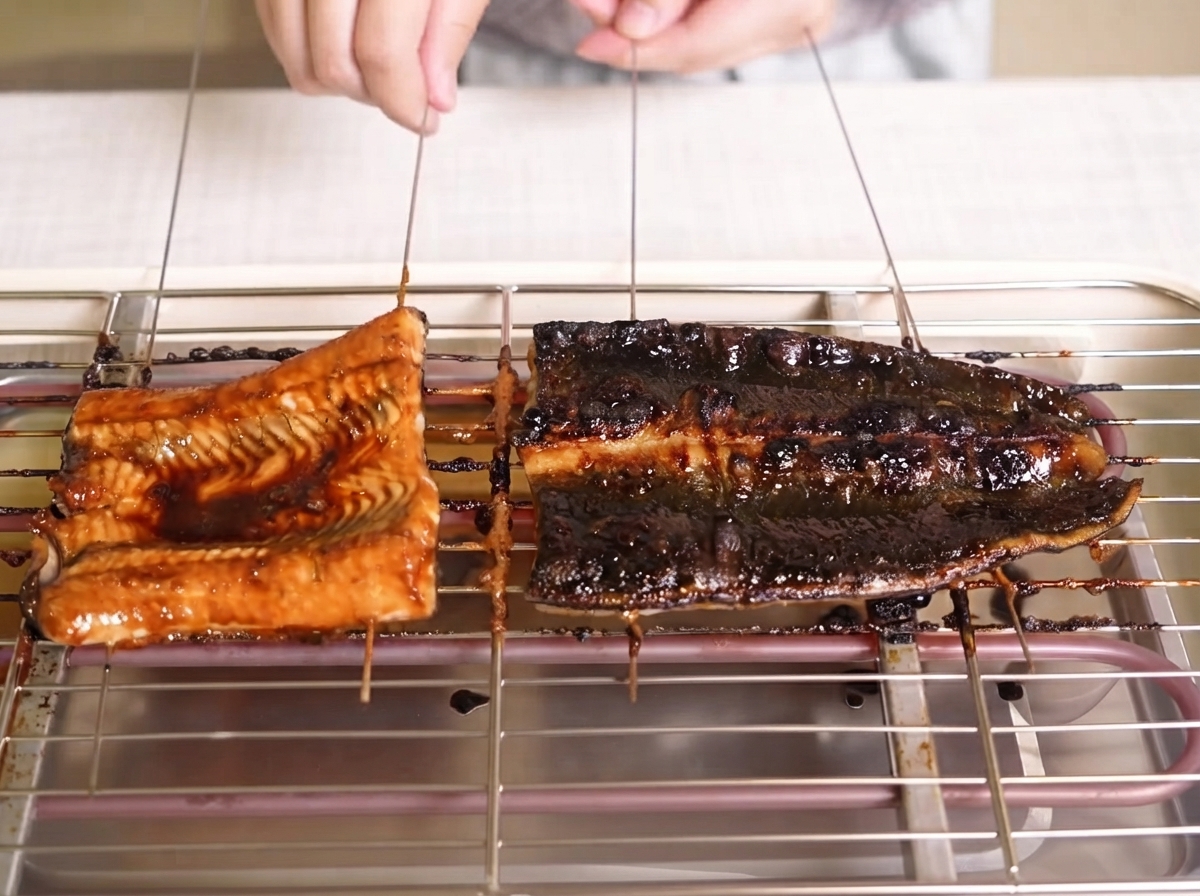 Bräunende Aalfilets werden auf einem Grillrost mit einer glänzenden, dunklen Sauce bestrichen.
