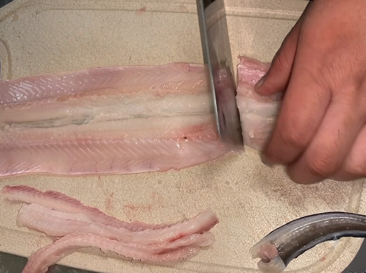 Ein Messer schneidet ein entgrätetes rohes Aalfilet auf einem Schneidebrett in zwei separate Abschnitte.