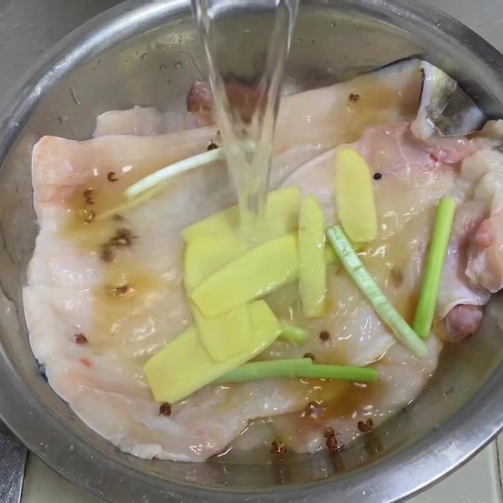 Klares Wasser wird in eine Metallschüssel mit Aalfilets, Ingwer, Frühlingszwiebeln und Sichuan-Pfefferkörnern gegossen.