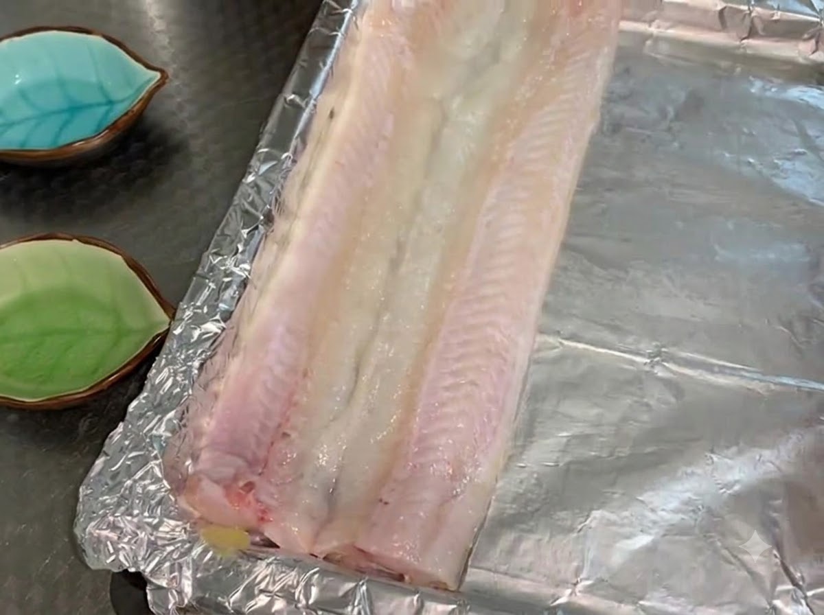 Rohe Aalfilets liegen flach in einer einzigen Schicht auf einem mit Öl bestrichenen, alufolienbedeckten Backblech.