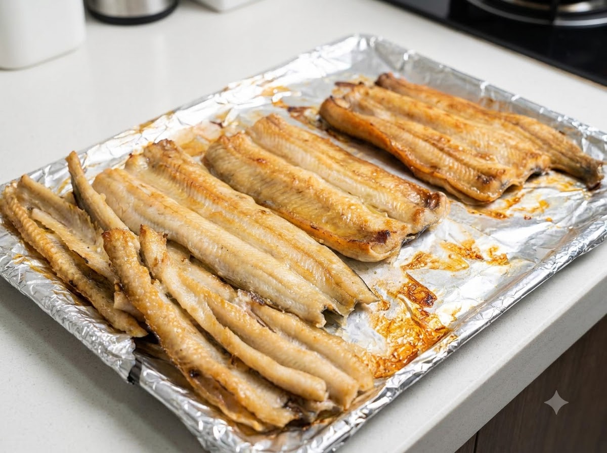 Nahaufnahme von teilweise gebackenen Aalfilets, die auf einem Backblech mit Speiseöl bestrichen werden.