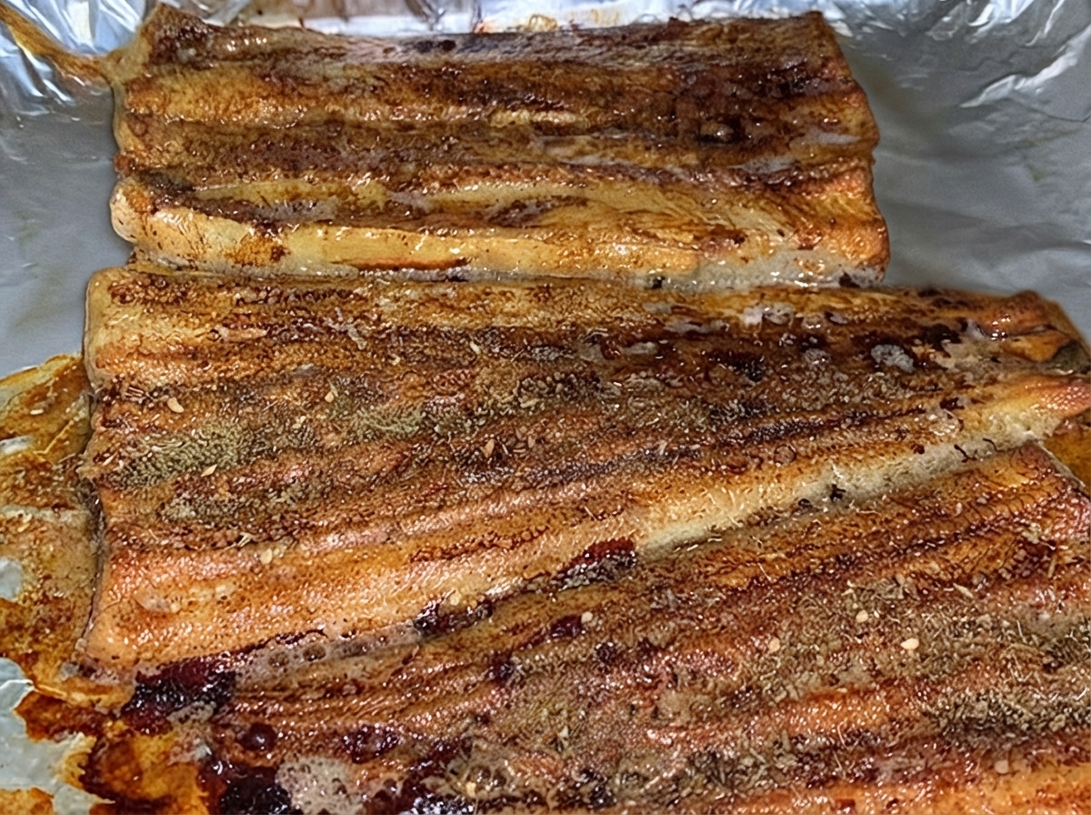 Gebackene Aalfilets, die gleichmäßig mit einer Schicht braunem BBQ-Gewürzpulver in einer Backform bestäubt sind.