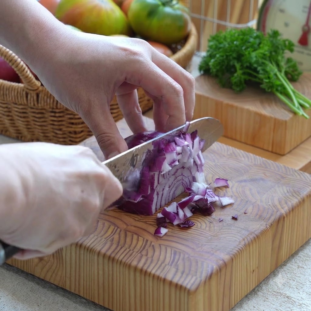 Rote Zwiebel wird mit einem Messer auf einem Holzbrett in kleine Stücke geschnitten.
