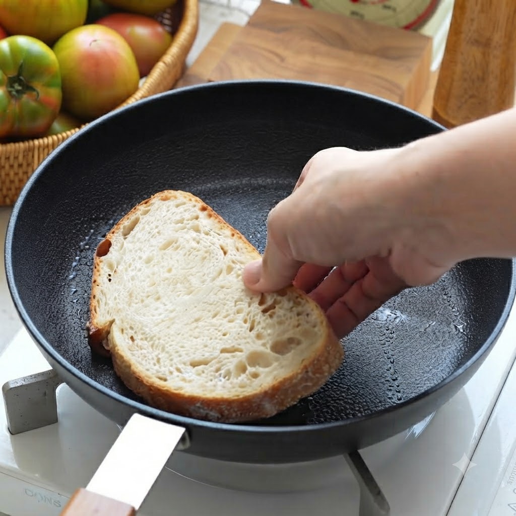 Eine Scheibe Sauerteigbrot wird zum Anbraten in eine schwarze Pfanne gelegt.