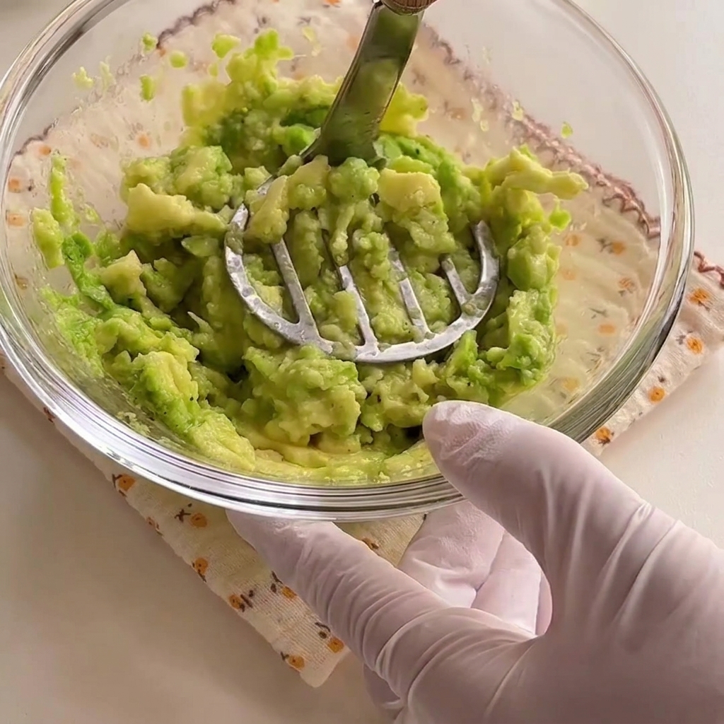 Avocadohälften werden mit einem Metallstampfer in einer Schüssel zu einer grünen Paste verarbeitet.