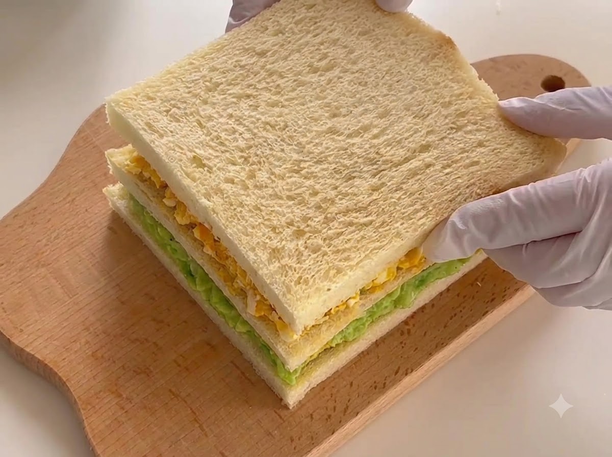 Das fertig zusammengesetzte dreischichtige Sandwich liegt bereit zum Schneiden auf einem Brett.