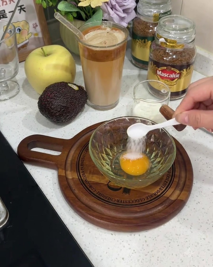 Ein kleiner weißer Löffel gibt Salz direkt auf das Eigelb eines rohen Eies in einer Glasschüssel.