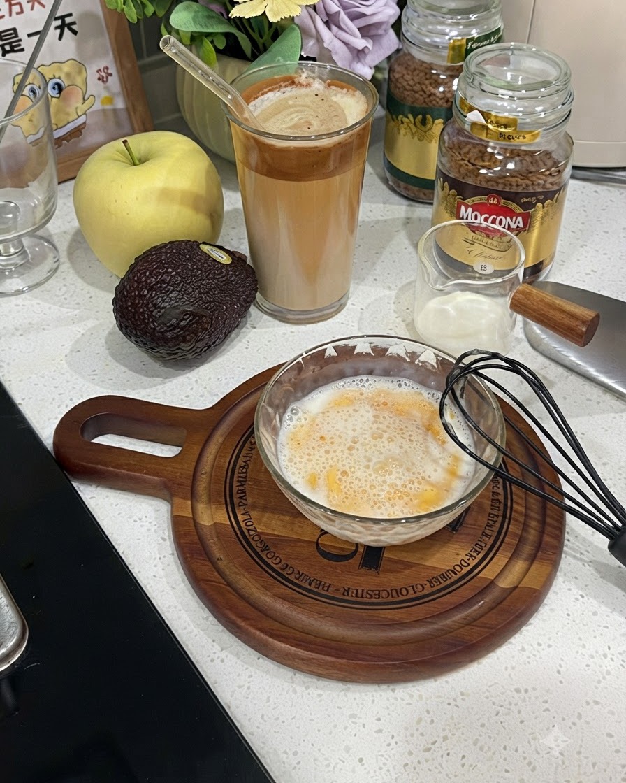 Eine Glasschüssel gefüllt mit einer schaumigen Ei-Milch-Mischung neben einem schwarzen Schneebesen.