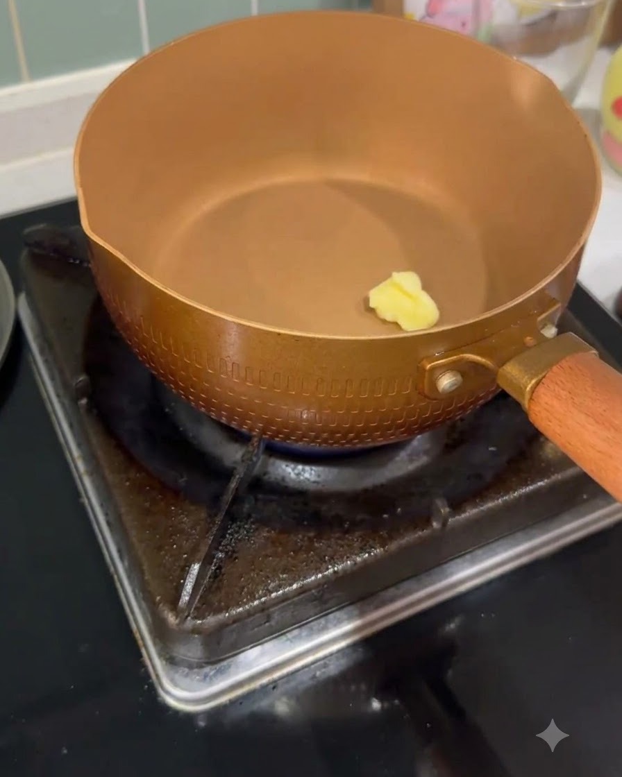 Ein kleines Stück Butter schmilzt in einer erhitzten, kupferfarbenen Pfanne auf einem Gasherd.