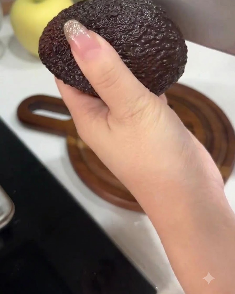 Eine Hand hält eine Avocado und schneidet sie mit einem großen Küchenmesser in der Mitte durch.
