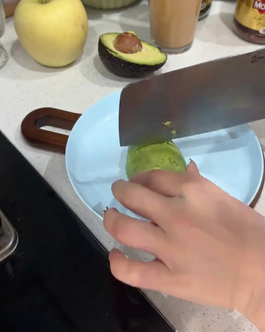 Eine Avocadoscheibe wird auf einem hellblauen Teller in dünne Stücke geschnitten.
