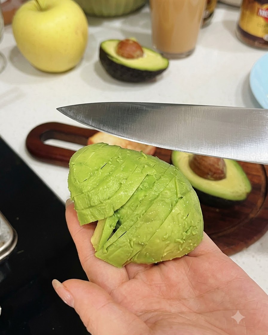 Eine Hand hält eine geschälte Avocadohälfte, während ein Küchenmesser sie in gleichmäßige Stücke schneidet.