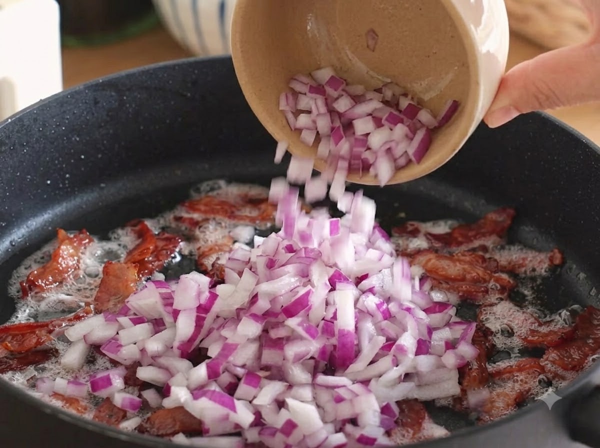 Gewürfelte rote Zwiebeln werden über den gebratenen Speck in die Pfanne gegeben.