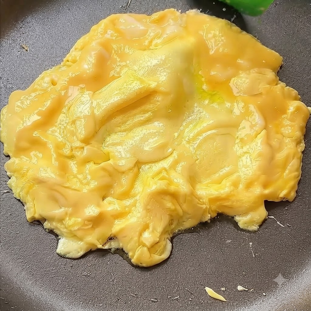 Eier werden mit einem Spatel in die Mitte der Pfanne geschoben.