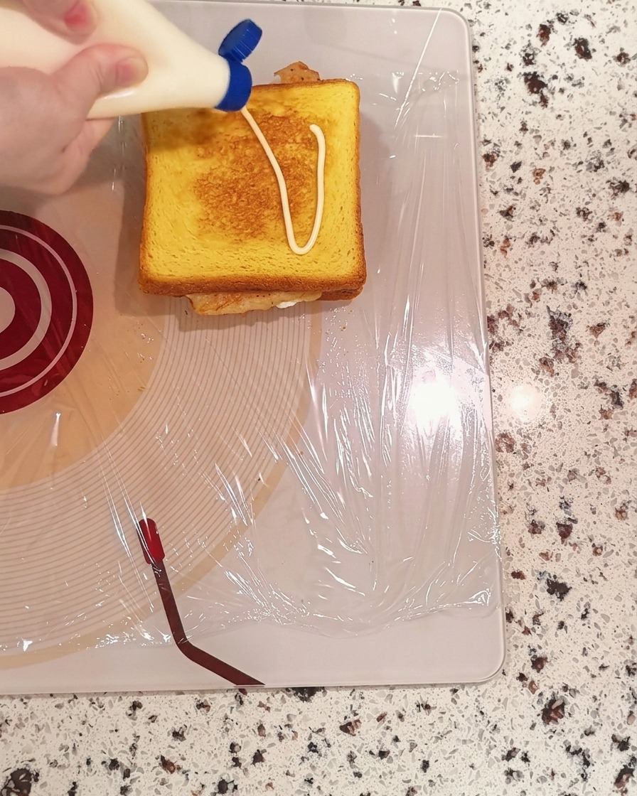 Mayonnaise wird in einem Zickzackmuster aus einer Flasche auf eine Scheibe Toastbrot gedrückt.