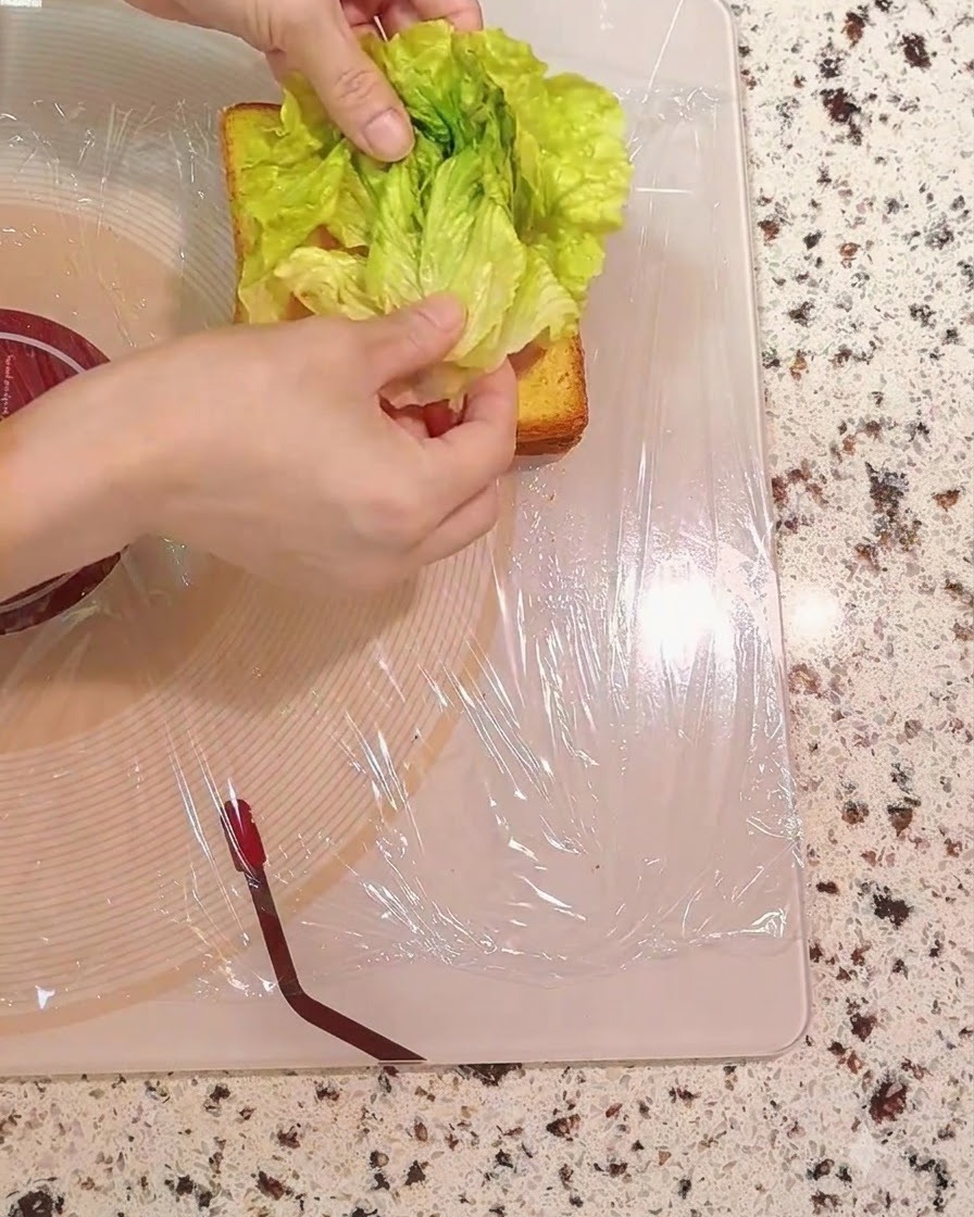 Frische grüne Salatblätter werden auf die Sandwichschichten gelegt.