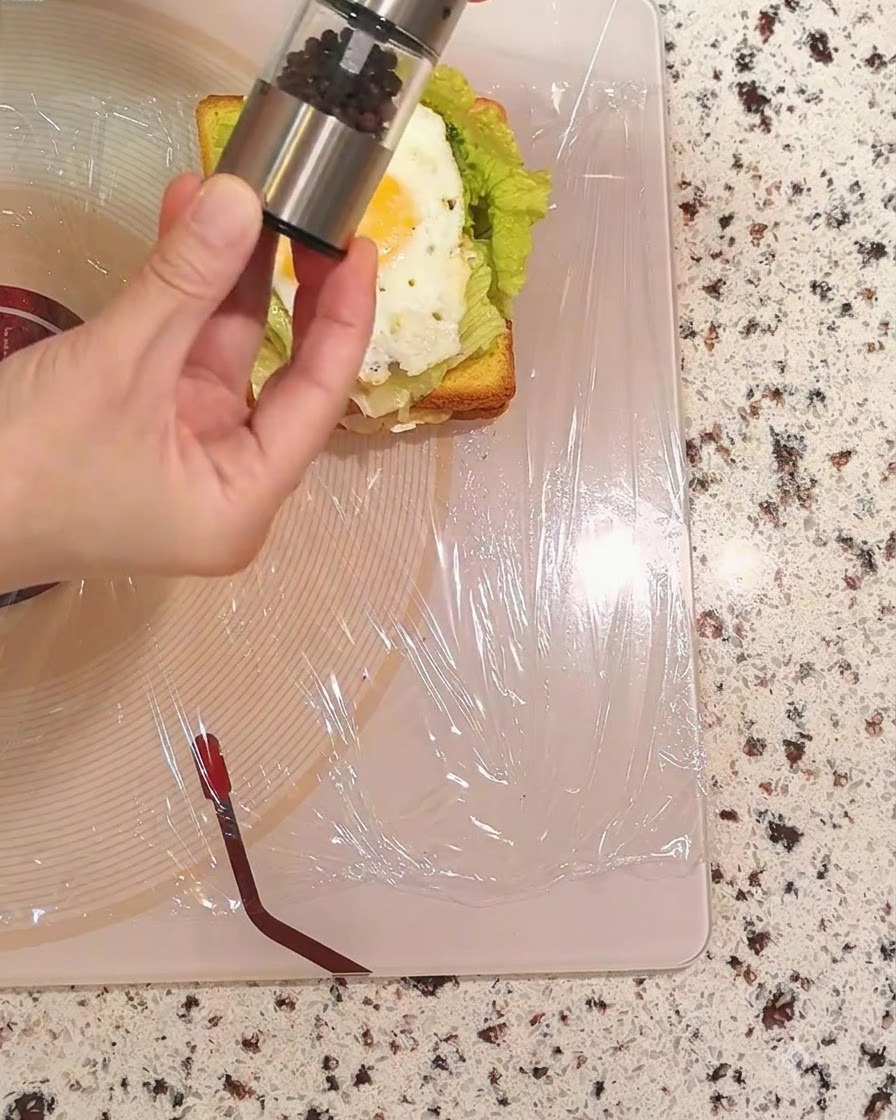 Eine Hand hält eine Pfeffermühle und streut schwarzen Pfeffer über das Spiegelei.