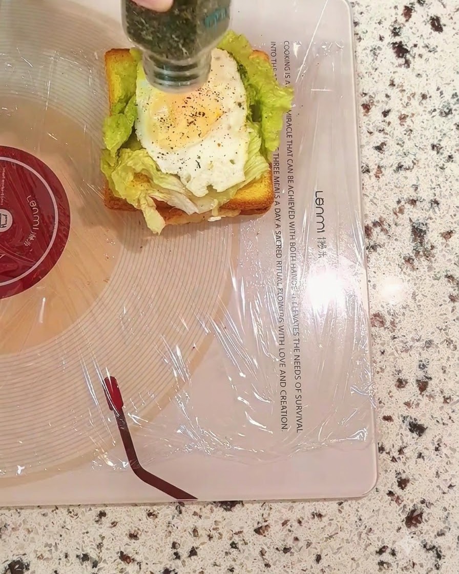 Getrocknete Petersilie wird aus einer Flasche auf die Eischicht des Sandwiches gestreut.