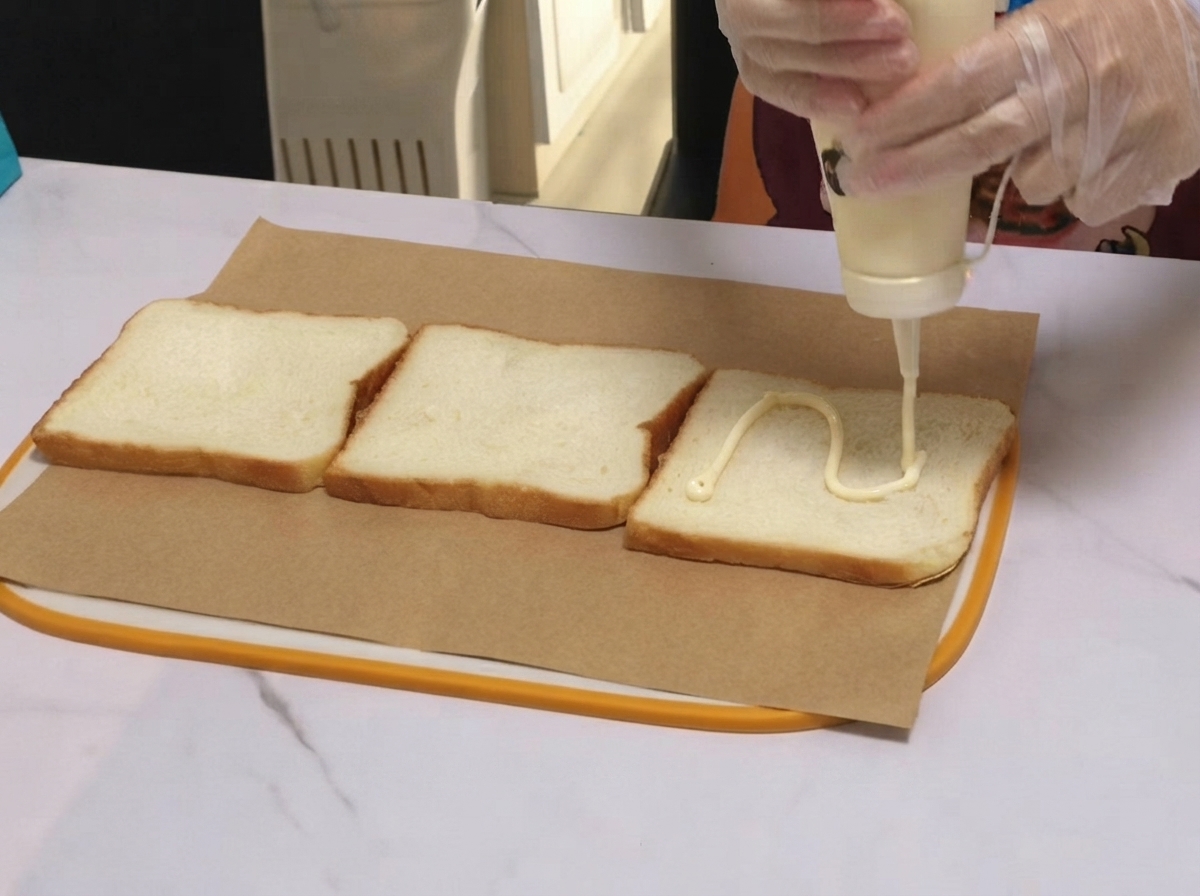 Weiße Salatcreme in Wellenlinie auf einer Weißbrotscheibe auf Backpapier.