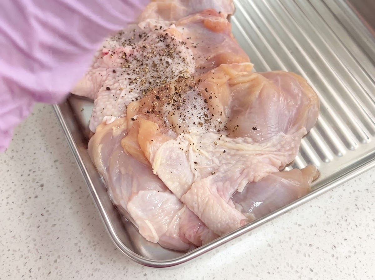 Entbeinte Hähnchenschenkel, gewürzt mit frisch gemahlenem schwarzem Pfeffer in einem Metallblech.