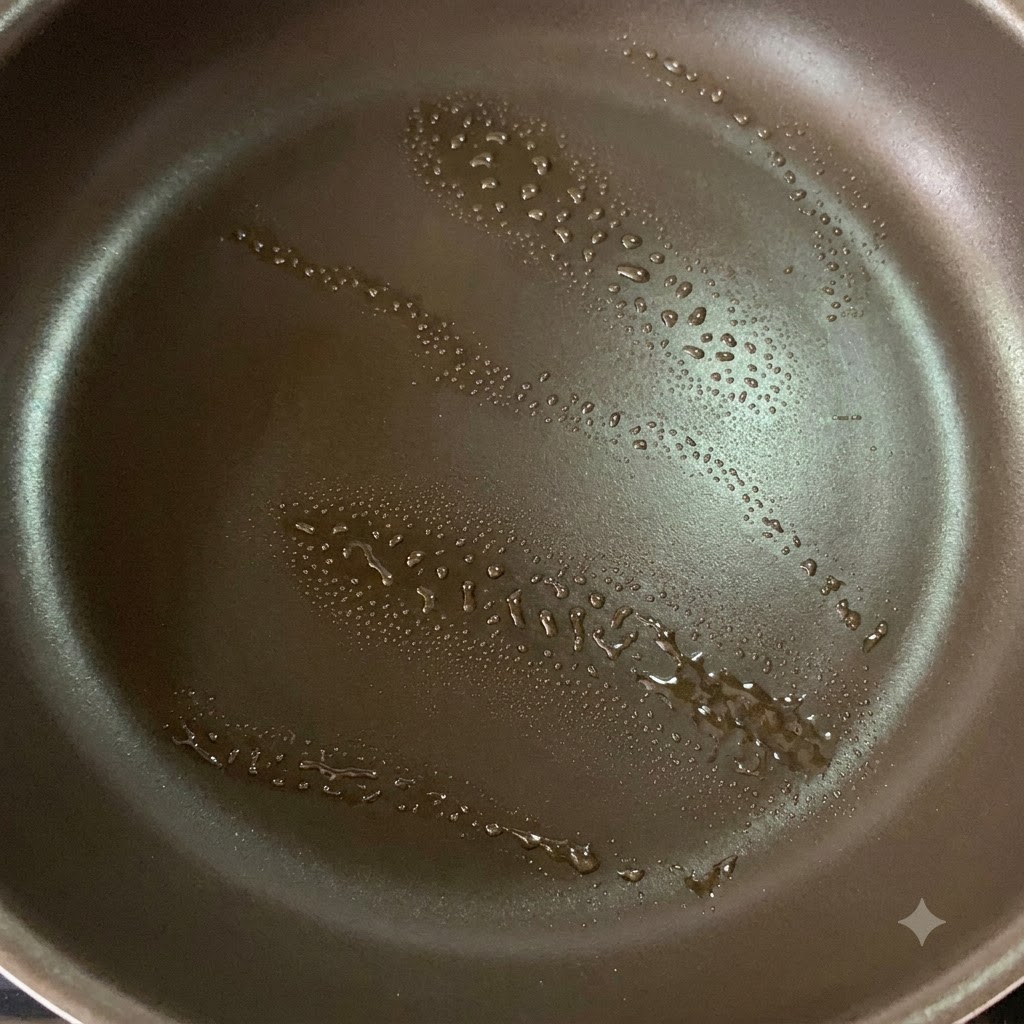 Eine Antihaft-Pfanne mit einem leichten Sprühstoß Öl, vorbereitet zum Anbraten von Hähnchenschenkeln.