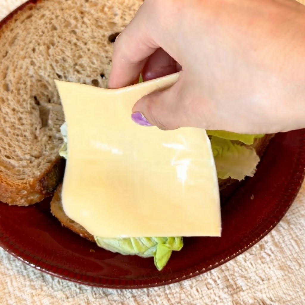 Zwei Scheiben gelber, fettreduzierter Käse werden sorgfältig über den knackig grünen Salat gelegt.
