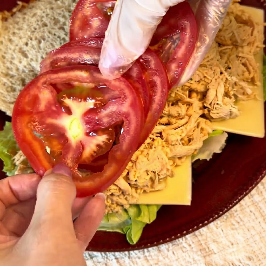 Frische rote Tomatenscheiben werden ordentlich über der zerkleinerten Hähnchenfüllung angeordnet.