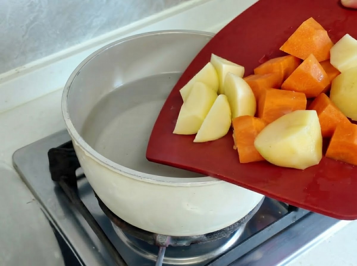 Kartoffel- und Karottenstücke kochen in einem Topf auf einer heißen Herdplatte.