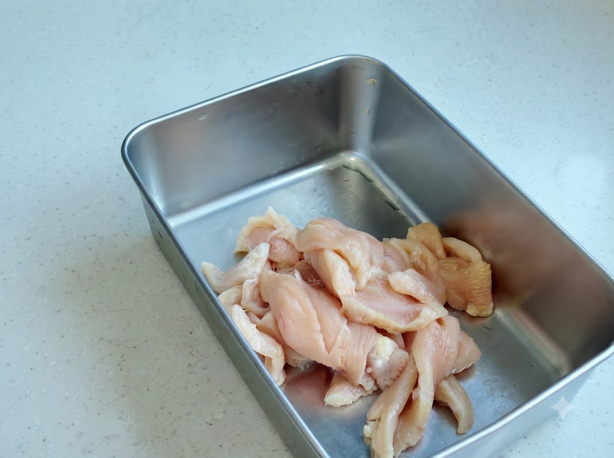 Geschnittenes Hähnchen in einem Metallbehälter mit verschiedenen Gewürzpulvern und Saucen.