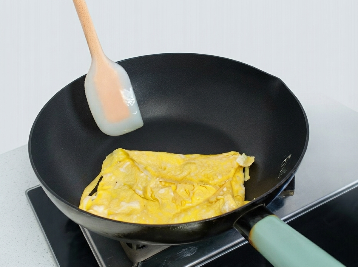 Ein teilweise gefaltetes Eieromelett in einer Bratpfanne wird mit einem Silikonspatel geformt.